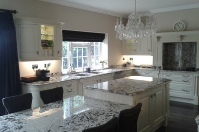 Large traditional u-shaped kitchen/diner in London with a submerged sink, raised-panel cabinets, granite worktops, stainless steel appliances, dark hardwood flooring, an island and white cabinets.