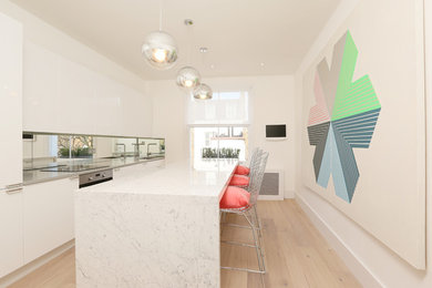 Moderne Küche mit Unterbauwaschbecken, flächenbündigen Schrankfronten, weißen Schränken, Rückwand aus Spiegelfliesen, Küchengeräten aus Edelstahl, hellem Holzboden und Kücheninsel in London