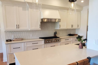 Inredning av ett modernt mellanstort vit vitt kök, med bänkskiva i kvarts, beige stänkskydd, stänkskydd i porslinskakel, rostfria vitvaror, mellanmörkt trägolv och en köksö