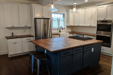 Enclosed kitchen - mid-sized country l-shaped dark wood floor and brown floor enclosed kitchen idea in Atlanta with a farmhouse sink, shaker cabinets, white cabinets, wood countertops, stainless steel appliances, an island and brown countertops