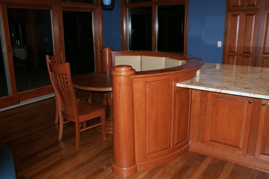 Example of a mid-sized classic l-shaped eat-in kitchen design in Other with raised-panel cabinets, medium tone wood cabinets, quartz countertops and an island