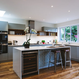 This is an example of a medium sized contemporary u-shaped kitchen in Surrey with flat-panel cabinets, grey cabinets, quartz worktops, stainless steel appliances, light hardwood flooring, an island, beige floors and white worktops.