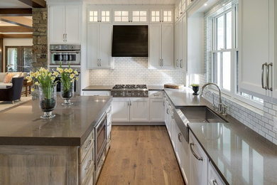 Inspiration for a mid-sized country u-shaped light wood floor and brown floor open concept kitchen remodel in Minneapolis with a farmhouse sink, shaker cabinets, white cabinets, white backsplash, subway tile backsplash, stainless steel appliances and an island