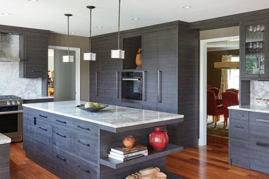Example of a trendy u-shaped medium tone wood floor and brown floor kitchen design in Baltimore with flat-panel cabinets, gray cabinets, white backsplash, stone slab backsplash, an island and white countertops