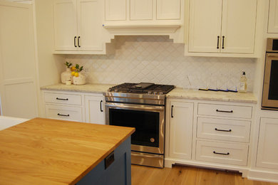 グランドラピッズにあるおしゃれなキッチン (エプロンフロントシンク、白いキャビネット、御影石カウンター、白いキッチンパネル) の写真