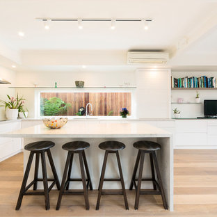 Contemporary l-shaped eat-in kitchen in Melbourne with an undermount sink, flat-panel cabinets, white cabinets, white splashback, window splashback, light hardwood floors, with island, beige floor and white benchtop.