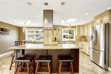 Klassisk inredning av ett stort kök, med en undermonterad diskho, luckor med lamellpanel, vita skåp, granitbänkskiva, stänkskydd i glaskakel, rostfria vitvaror, klinkergolv i keramik och en köksö
