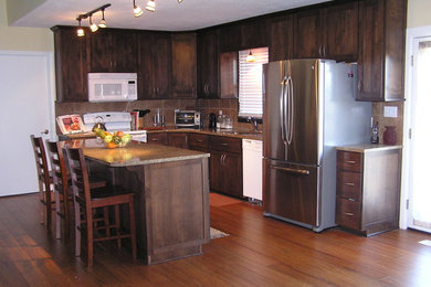 Eat-in kitchen - mid-sized mediterranean l-shaped medium tone wood floor and brown floor eat-in kitchen idea in Kansas City with an undermount sink, shaker cabinets, dark wood cabinets, granite countertops, brown backsplash, ceramic backsplash, white appliances and an island