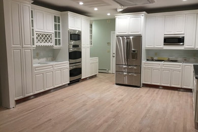 Large elegant u-shaped light wood floor and beige floor open concept kitchen photo in New York with flat-panel cabinets, white cabinets, white backsplash, cement tile backsplash, stainless steel appliances and no island