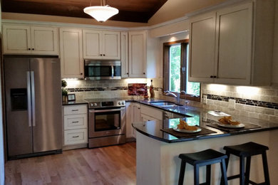 Classic u-shaped kitchen/diner in Minneapolis with a submerged sink, recessed-panel cabinets, distressed cabinets, granite worktops, multi-coloured splashback, stone tiled splashback, stainless steel appliances, medium hardwood flooring, a breakfast bar, brown floors and black worktops.