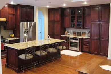 Example of a l-shaped light wood floor eat-in kitchen design in Kansas City with a single-bowl sink, shaker cabinets, dark wood cabinets, granite countertops, beige backsplash, ceramic backsplash, stainless steel appliances and an island