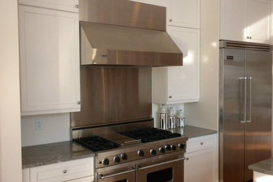 This is an example of a contemporary u-shaped kitchen/diner in New York with flat-panel cabinets, granite worktops, beige splashback, white cabinets, stainless steel appliances and a submerged sink.