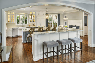 Example of a large classic u-shaped medium tone wood floor and brown floor eat-in kitchen design in Dallas with a farmhouse sink, white cabinets, quartzite countertops, an island, shaker cabinets, white backsplash, ceramic backsplash, paneled appliances and multicolored countertops