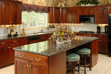 Mid-sized elegant l-shaped enclosed kitchen photo in Philadelphia with an undermount sink, raised-panel cabinets, medium tone wood cabinets, granite countertops, white backsplash, black appliances and an island