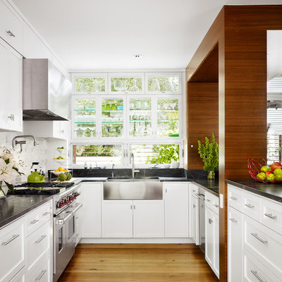 Mid-century modern kitchen photo in Austin with stainless steel appliances, a farmhouse sink, recessed-panel cabinets, white cabinets, white backsplash and stone tile backsplash