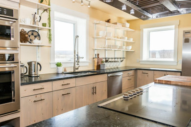 Inspiration for a large l-shaped cork floor and brown floor kitchen remodel in Other with light wood cabinets, stainless steel appliances, an island, black countertops, an undermount sink, flat-panel cabinets and quartzite countertops