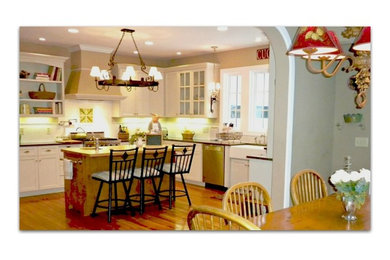 Mid-sized elegant l-shaped medium tone wood floor eat-in kitchen photo in Minneapolis with a farmhouse sink, glass-front cabinets, white cabinets, granite countertops, white backsplash, subway tile backsplash, stainless steel appliances and an island