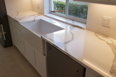 Inspiration for a large contemporary galley porcelain tile and gray floor eat-in kitchen remodel in Miami with a farmhouse sink, shaker cabinets, white cabinets, quartz countertops, stainless steel appliances, a peninsula and white countertops