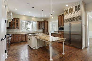 Trendy u-shaped medium tone wood floor kitchen photo in Boston with raised-panel cabinets, medium tone wood cabinets, granite countertops, white backsplash, stainless steel appliances and an island