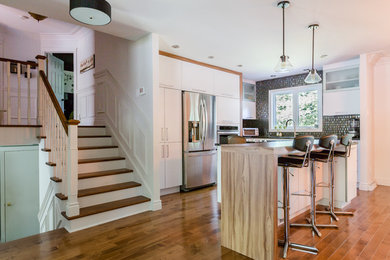 Moderne Küche in U-Form mit flächenbündigen Schrankfronten, weißen Schränken, Küchenrückwand in Metallic, Küchengeräten aus Edelstahl, braunem Holzboden und Kücheninsel in Montreal