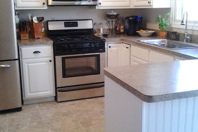 Example of a mid-sized transitional u-shaped beige floor eat-in kitchen design in Grand Rapids with a double-bowl sink, raised-panel cabinets, white cabinets, laminate countertops, gray backsplash, stainless steel appliances and no island