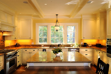Cette photo montre une cuisine américaine moderne avec un placard avec porte à panneau surélevé, des portes de placard beiges, un plan de travail en granite, une crédence marron et une crédence en carrelage de pierre.