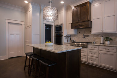 Example of a large transitional u-shaped concrete floor kitchen design in New Orleans with shaker cabinets, dark wood cabinets, granite countertops, beige backsplash, stone tile backsplash, stainless steel appliances and an island