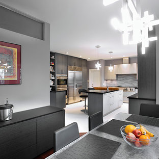 Modelo de cocina comedor en U, moderna, grande, con armarios con paneles lisos, puertas de armario grises, encimera de acrílico, salpicadero metalizado, salpicadero de metal, electrodomésticos de acero inoxidable, suelo laminado y una isla