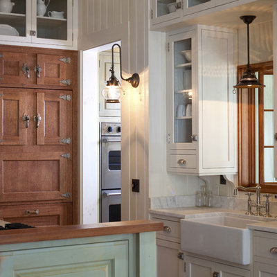 Example of a mid-sized beach style galley enclosed kitchen design in Other with glass-front cabinets, a farmhouse sink, marble countertops, white cabinets, stainless steel appliances and an island