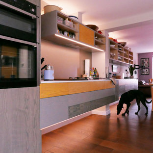 Inspiration for a mid-sized contemporary galley open plan kitchen in London with an integrated sink, flat-panel cabinets, yellow cabinets, laminate benchtops, metallic splashback, stainless steel appliances, medium hardwood floors, with island, brown floor and white benchtop.