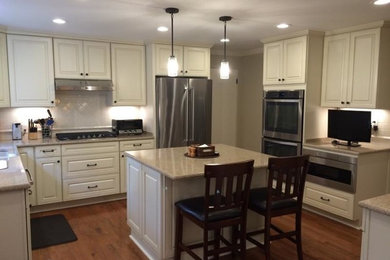 Example of a large classic u-shaped dark wood floor enclosed kitchen design in Other with a double-bowl sink, raised-panel cabinets, white cabinets, white backsplash, subway tile backsplash, stainless steel appliances and an island