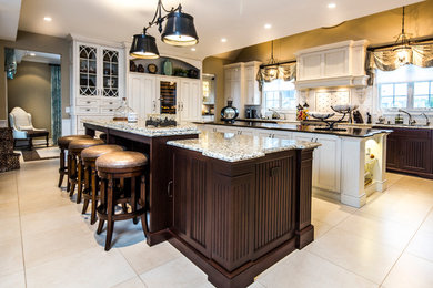Example of a large transitional l-shaped limestone floor and beige floor kitchen design in New York with an undermount sink, beaded inset cabinets, white cabinets, granite countertops, beige backsplash, matchstick tile backsplash, paneled appliances and two islands