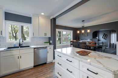 Inspiration for a large industrial u-shaped medium tone wood floor and brown floor eat-in kitchen remodel in Other with a drop-in sink, recessed-panel cabinets, white cabinets, marble countertops, white backsplash, subway tile backsplash, black appliances, an island and white countertops