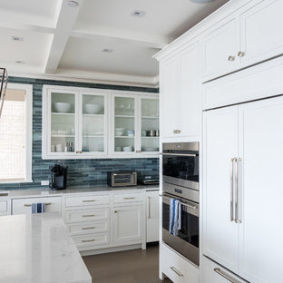 Foto di una cucina costiera di medie dimensioni con lavello sottopiano, ante di vetro, ante bianche, paraspruzzi blu, paraspruzzi con piastrelle di vetro, elettrodomestici in acciaio inossidabile, pavimento in legno massello medio, isola, pavimento marrone e top bianco