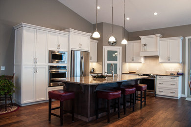 Example of a mid-sized arts and crafts u-shaped medium tone wood floor eat-in kitchen design in Calgary with a drop-in sink, raised-panel cabinets, white cabinets, granite countertops, beige backsplash, subway tile backsplash, stainless steel appliances and an island