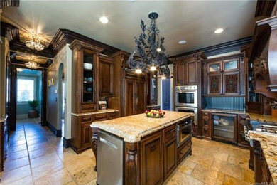 トラディショナルスタイルのおしゃれなキッチン (エプロンフロントシンク、レイズドパネル扉のキャビネット、黒いキッチンパネル、木材のキッチンパネル、パネルと同色の調理設備、トラバーチンの床、ベージュの床) の写真