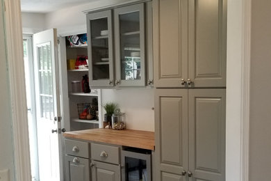 Example of a classic galley laminate floor and brown floor kitchen pantry design in Other with raised-panel cabinets, gray cabinets, wood countertops and no island