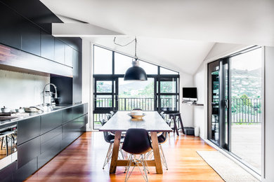 Imagen de cocina comedor lineal minimalista pequeña con puertas de armario negras, encimera de acero inoxidable, salpicadero verde y suelo de madera en tonos medios