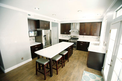 Example of a mid-sized transitional u-shaped medium tone wood floor eat-in kitchen design in Los Angeles with dark wood cabinets, granite countertops, green backsplash, stainless steel appliances, an island, a double-bowl sink, recessed-panel cabinets and ceramic backsplash