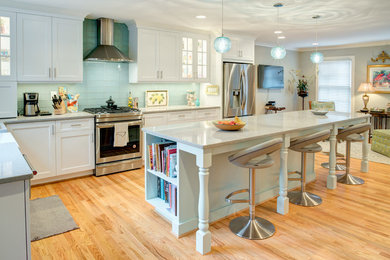 Example of a trendy light wood floor eat-in kitchen design in Raleigh with a farmhouse sink, glass-front cabinets, white cabinets, quartzite countertops, blue backsplash, glass tile backsplash, stainless steel appliances, an island and gray countertops
