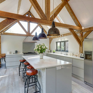 Design ideas for a farmhouse l-shaped kitchen in Kent with a double-bowl sink, flat-panel cabinets, grey cabinets, stainless steel appliances, an island and grey floors.