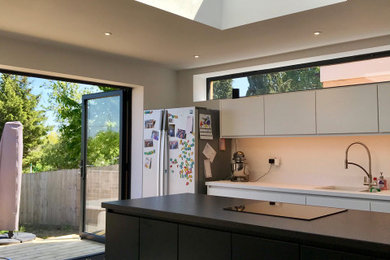 This is an example of a large contemporary single-wall kitchen/diner in Oxfordshire with flat-panel cabinets, white cabinets, laminate countertops, vinyl flooring, an island, brown floors and white worktops.