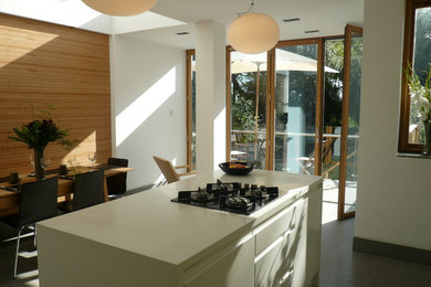 This is an example of a medium sized modern galley open plan kitchen in Manchester with flat-panel cabinets, white cabinets, composite countertops, green splashback, glass sheet splashback and multiple islands.