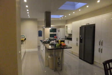 Photo of a large galley kitchen/diner in Other with a double-bowl sink, flat-panel cabinets, white cabinets, composite countertops, metallic splashback, metal splashback, integrated appliances, ceramic flooring and an island.