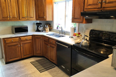 Example of a mid-sized classic u-shaped ceramic tile and gray floor enclosed kitchen design in New York with an undermount sink, raised-panel cabinets, medium tone wood cabinets, quartzite countertops, gray backsplash, glass tile backsplash, stainless steel appliances, no island and gray countertops