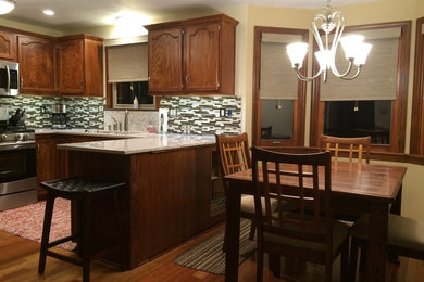 Transitional medium tone wood floor eat-in kitchen photo in Other with an undermount sink, recessed-panel cabinets, medium tone wood cabinets, quartz countertops, brown backsplash, glass tile backsplash and stainless steel appliances