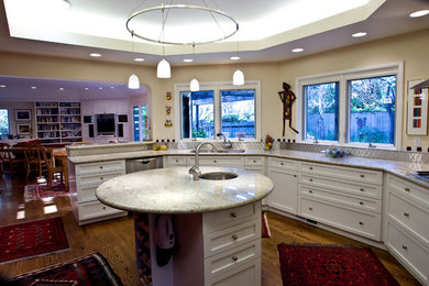 This is an example of a medium sized contemporary u-shaped kitchen/diner in San Francisco with a double-bowl sink, recessed-panel cabinets, white cabinets, granite worktops, metallic splashback, stainless steel appliances, medium hardwood flooring, an island, brown floors and white worktops.
