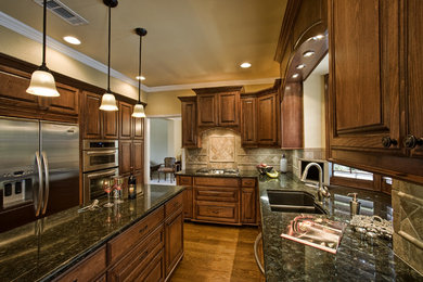 Example of a large classic galley dark wood floor and brown floor enclosed kitchen design in Dallas with a double-bowl sink, raised-panel cabinets, dark wood cabinets, granite countertops, beige backsplash, stone tile backsplash, stainless steel appliances and an island