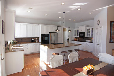 Bild på ett lantligt kök och matrum, med en dubbel diskho, skåp i shakerstil, vita skåp, granitbänkskiva, grått stänkskydd, stänkskydd i keramik, rostfria vitvaror, mellanmörkt trägolv och en köksö