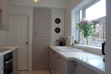 Inspiration for a small traditional galley enclosed kitchen in West Midlands with recessed-panel cabinets, grey cabinets, no island, white worktops, a belfast sink, grey splashback, ceramic splashback, stainless steel appliances, laminate floors and brown floors.
